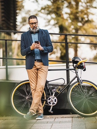 Casual businessman on his phone texting while leaning up against his bicycle.