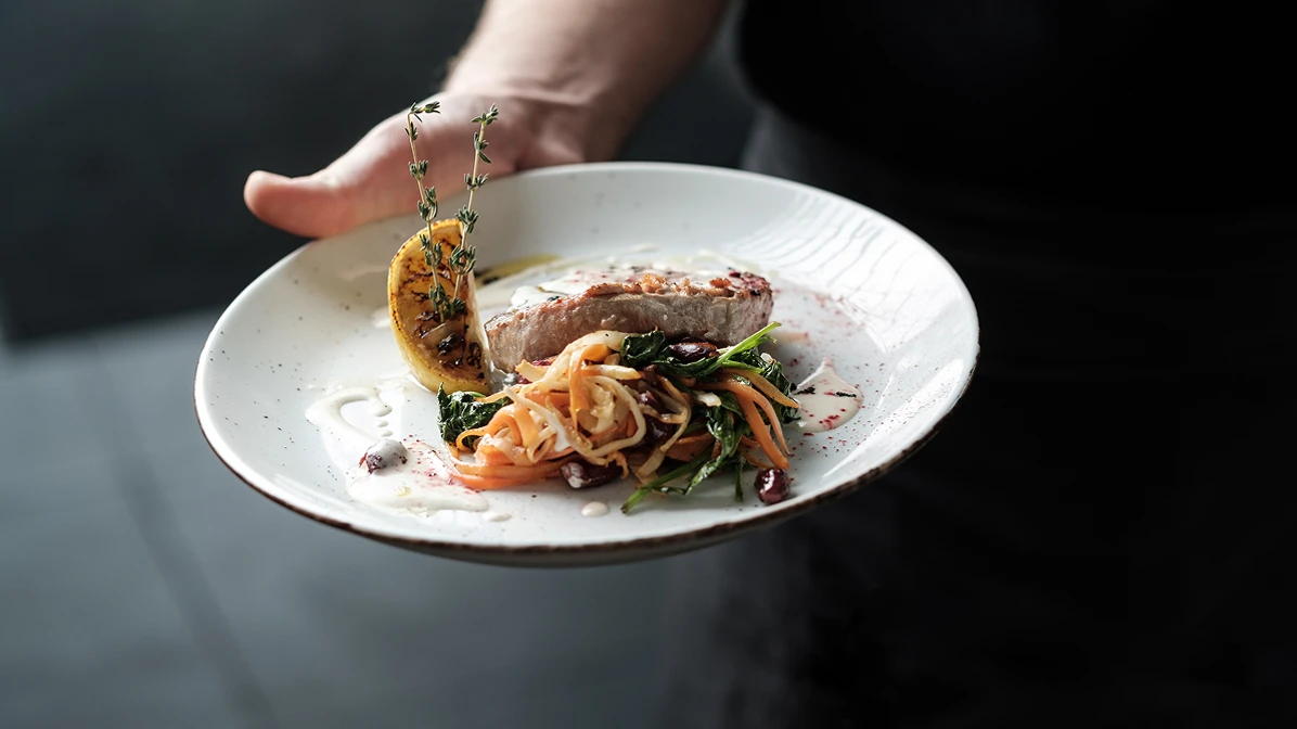 Closeup of hand holding out a food dish of fish and salad.
