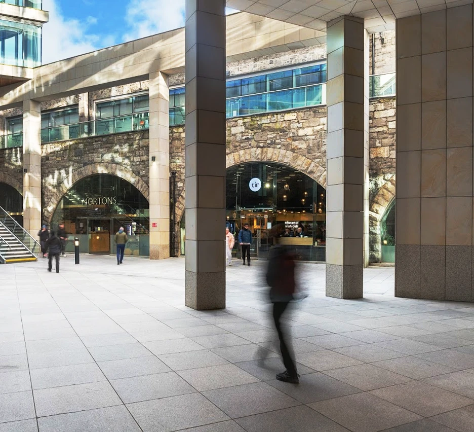 Man walking through the outside Vault area of the campus with shops in the background.