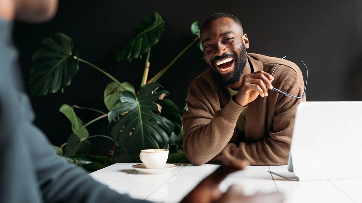 Man laughing with a work colleague as they enjoy a coffee break.