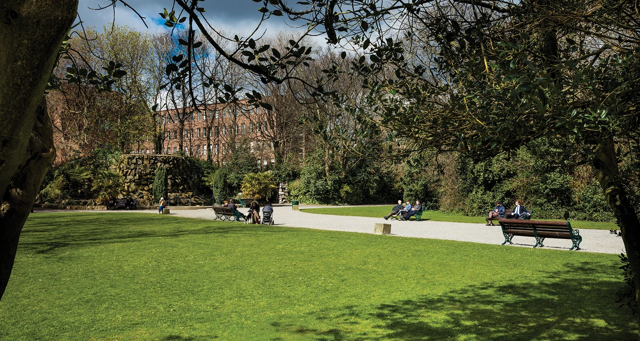 Iveagh Gardens green space with people sat on park benches.