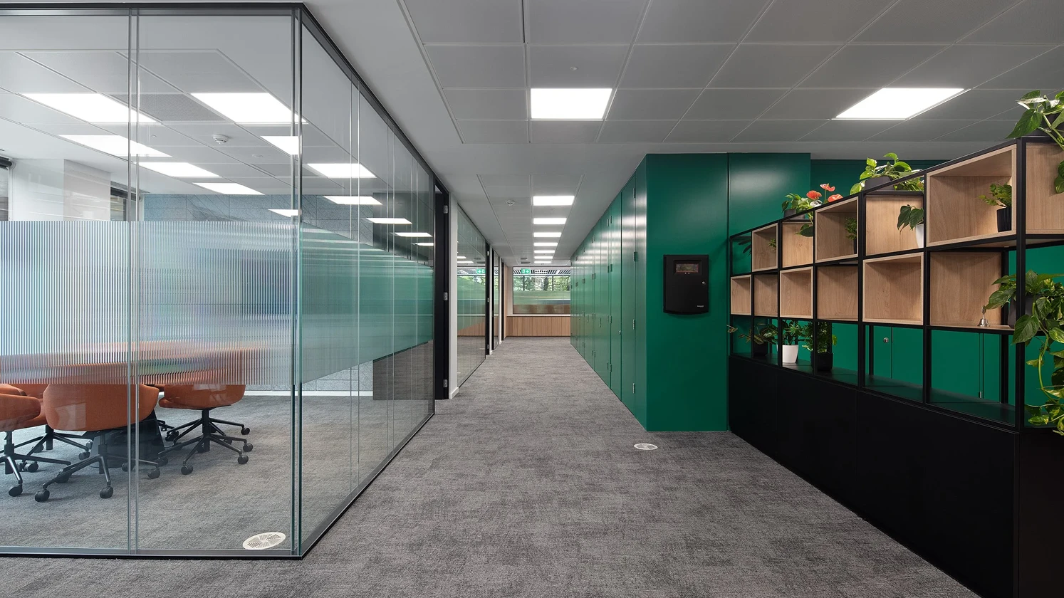 Workspace corridor with a glass meeting room on the left and green wall on the right.