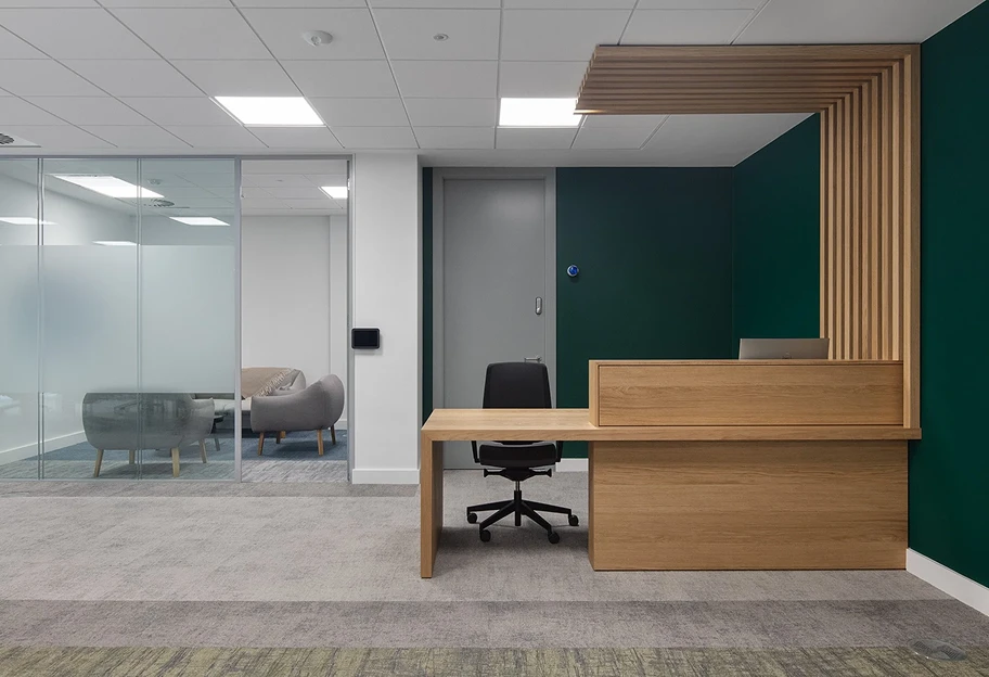 Reception with wooden desk, green walls and glass meeting room behind it.