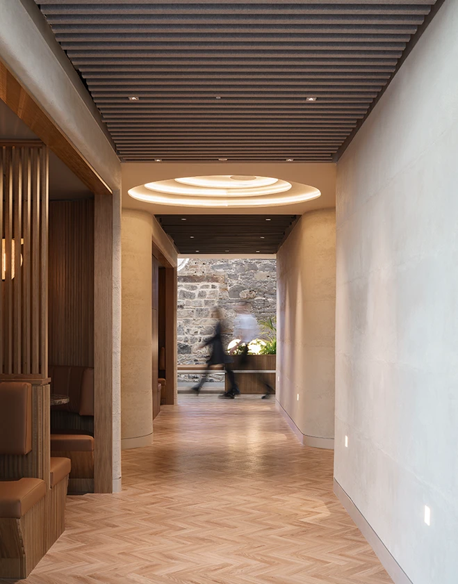 People passing the opening at the end of a long office hallway.