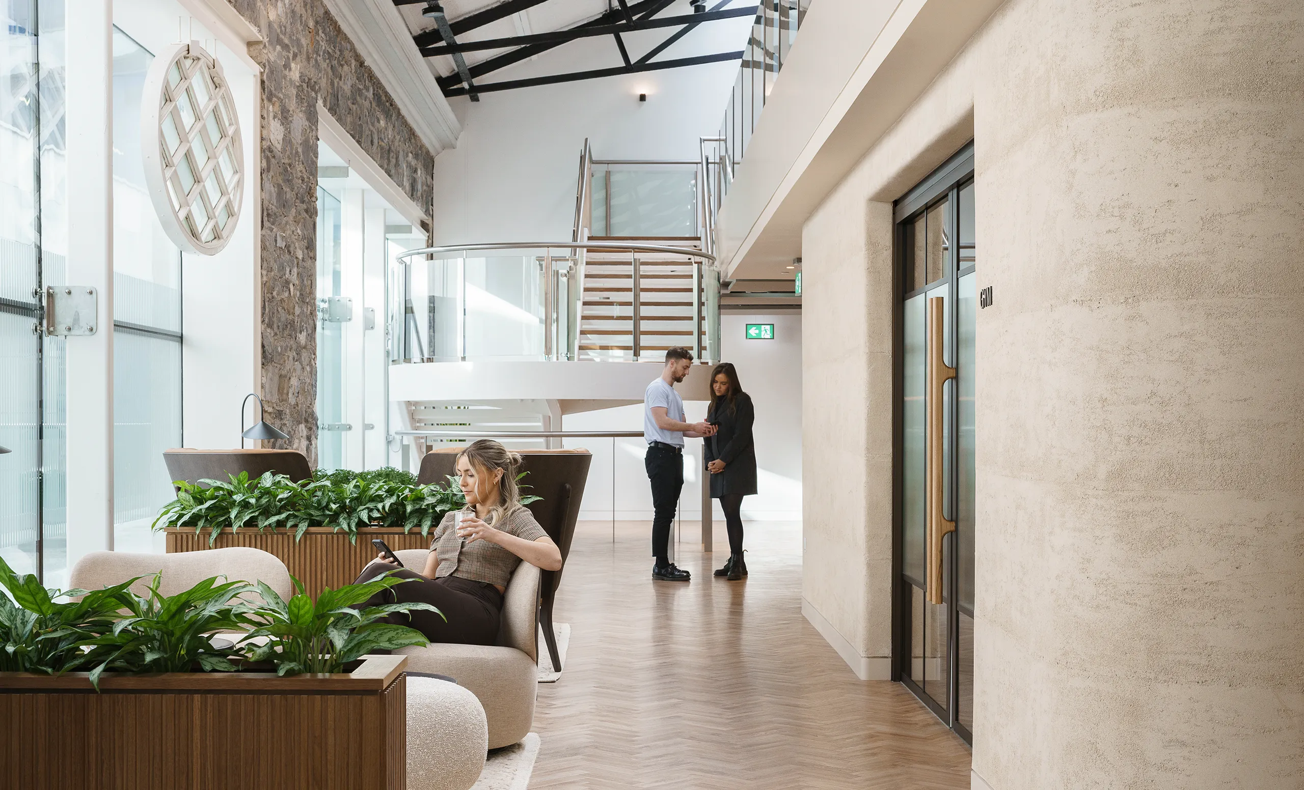 Beautiful open space workspace with a woman sat on her phone with a man and woman talking in the background.