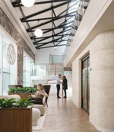 Beautiful open space workspace with a woman sat on her phone with a man and woman talking in the background.
