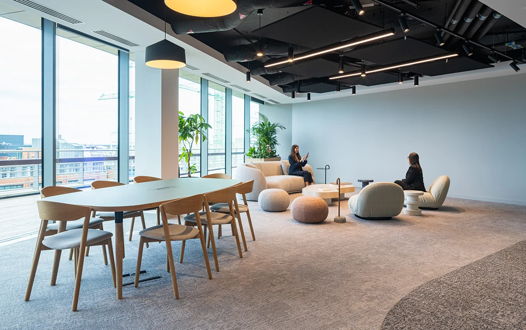 Two women sitting on comfy chairs by windows in a workspace breakout space.